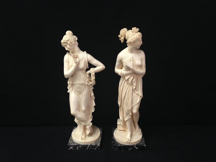 (2) Signed RUGGERI Alabaster/Resin Statues.: The beautiful vintage statues in this lot are a deep ivory color and composed of Alabaster/Resin and mounted to 4" square black marble pedestal. The statues of Greek/Roman Women stand about 14-1/2" to