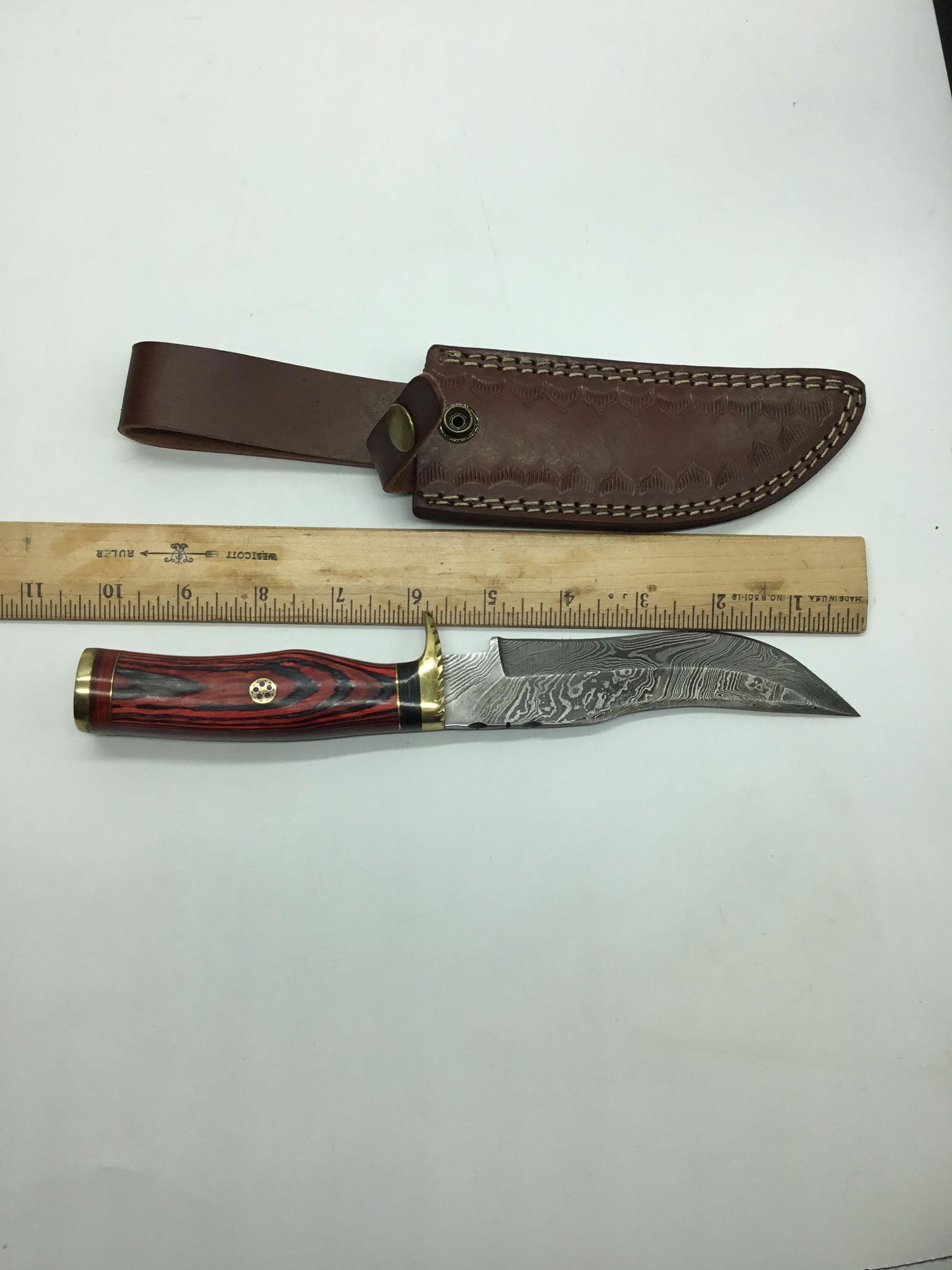 Damascus steel knife: Damascus steel knife with 5 1/2 inch blade, 4 1/2 inch brass and redwood handle. In leather sheath.