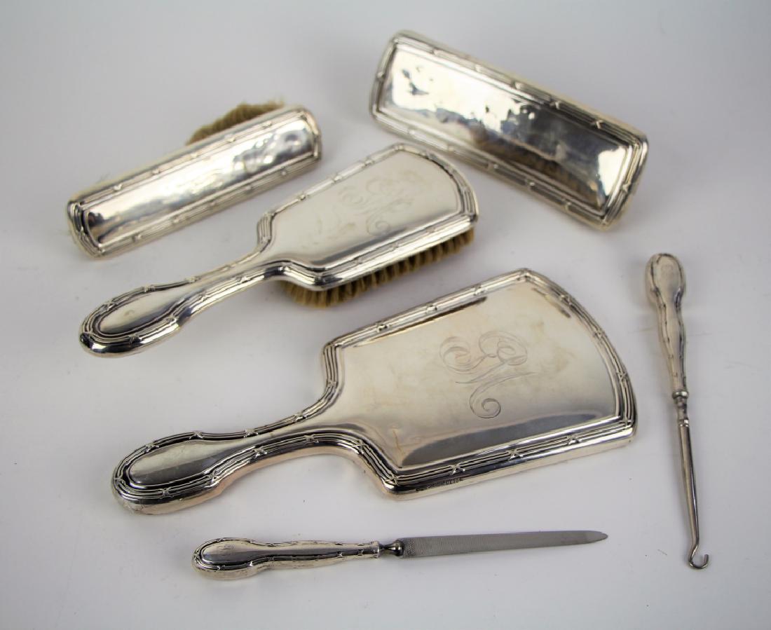 SILVER VANITY SET: Including hand mirror, three brushes, boot hook, and nail file. With crossed reeded design and monogrammed. Condition some dents. L. of mirror 25 cm (9 3/4 in.). Total approx. weight 890 g.