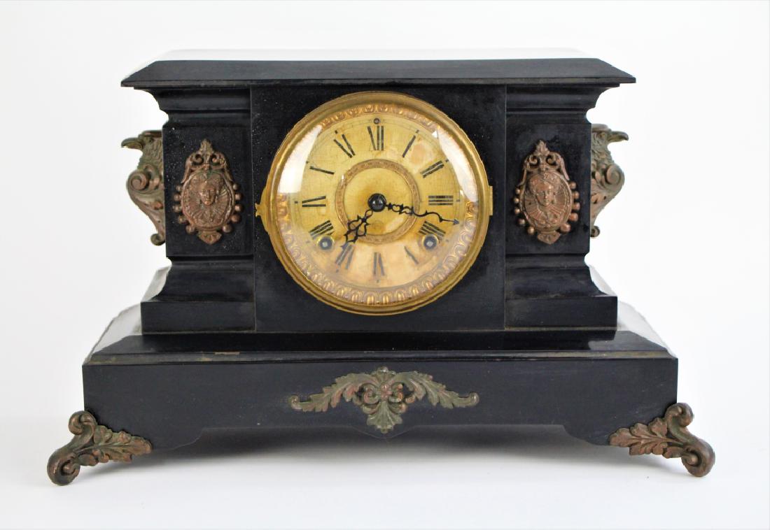 19TH C CAST METAL MANTLE CLOCK: Heavy cast metal clock with figural applique. Made by Ansonia Clock Co. With key and pendulum. Discolouration to face. L. 43 cm (16 3/4 in.)