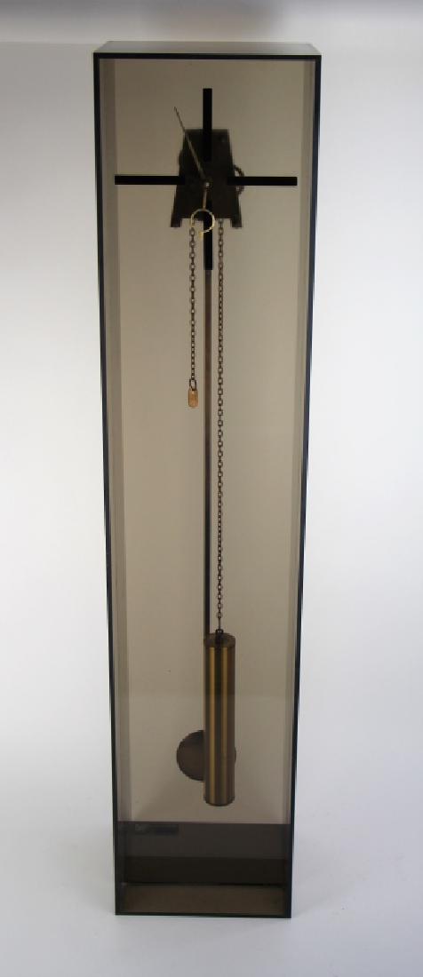 MID CENTURY ACRYLIC GRANDDAUGHTER CLOCK: Works stamped Made in Germany, designed and manufactured by 1984 Store Inc. Smoked acrylic and brass. Condition note, wire to hold top of pendulum off. H. 70.5 cm (42 1/4 in.).
