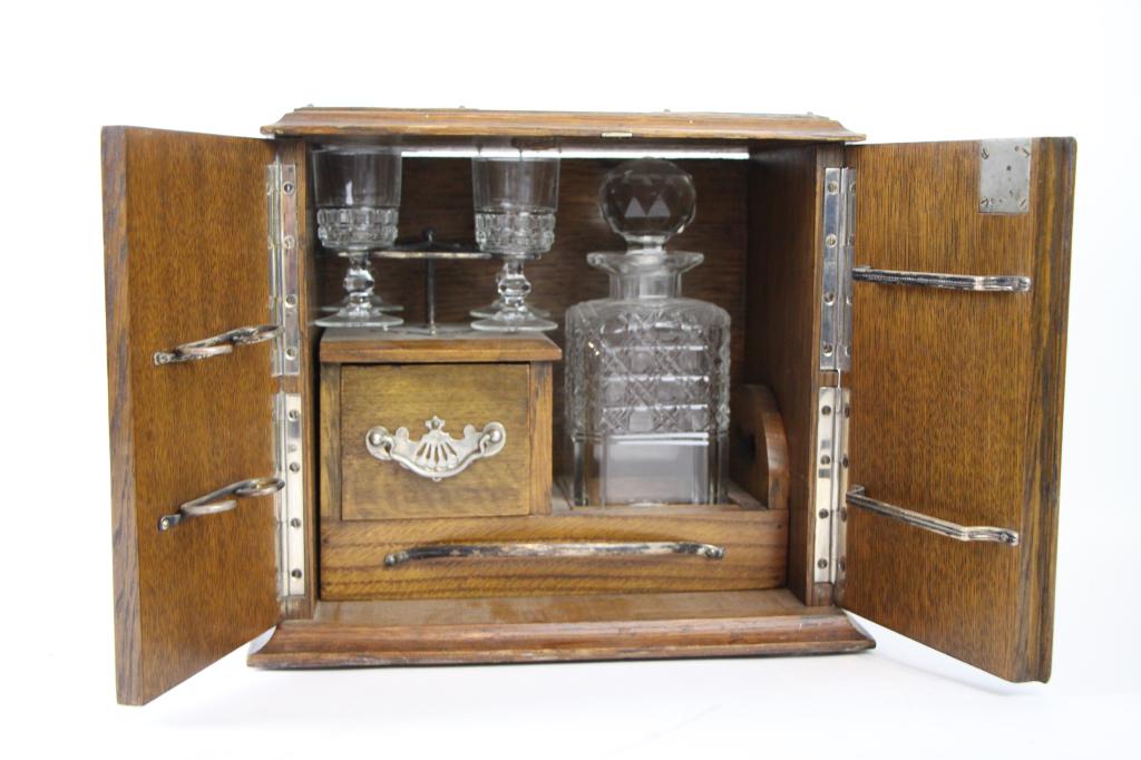 ANTIQUE DRINK CABINET / TANTALUS: Solid oak case, with ornate hardware. Pull out drawer holding decanter and glasses. In excellent condition. H: 11" W: 11 1/2" D: 8"
