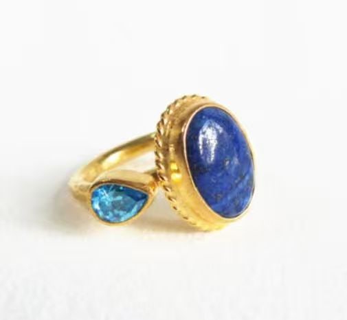 GOLD AND LAPIS LAZULI RING: GOLD AND LAPIS LAZULI RING Description: A yellow-metal ring centered by a polished oval lapis lazuli stone in a raised bezel, accompanied by a smaller pear-shaped blue stone set alongside the shank.