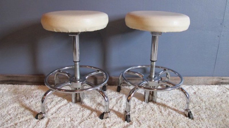 109. Machine Age Rolling Stools: A sweet pair of Machine Age Rolling Stools. Each with telescopic adjustable seats that rise and fall by spinning the stool seat. One stool being sold "as found" with a some damage to the "pleather" fa