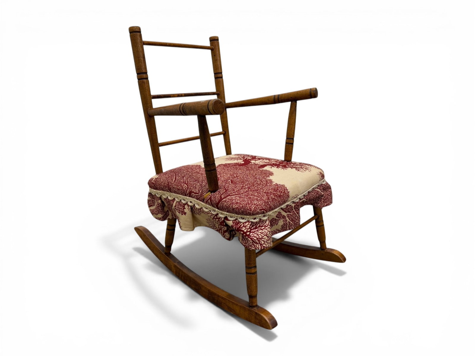 Miniature Upholstered Rocking Chair with Lace: A Miniature Upholstered Rocking Chair with Lace. The fabric is a red and beige botanical pattern. Dimensions: H:24.75" W:16.5" D:23.5" Seat Height:12"