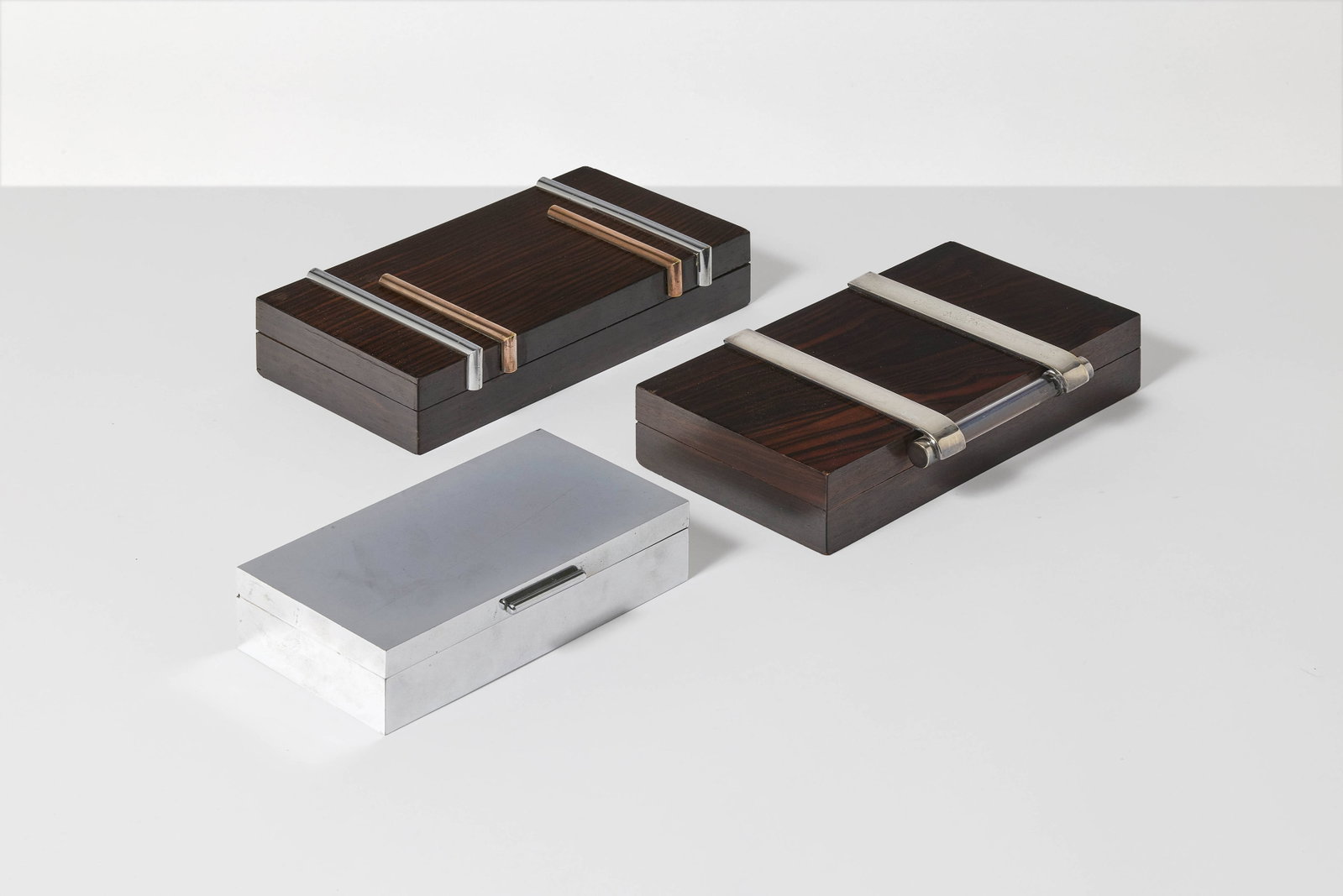 DESNY: DESNY Ensemble de trois boîtes à cigarette – circa 1930 Structure en chêne, placage en ébène de Macassar, sipo, laiton, laiton nickelé et verre 4,5 × 20,5 