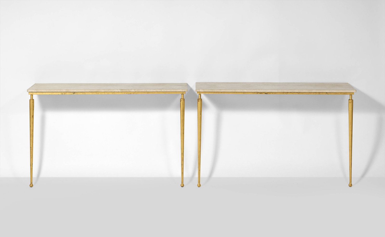 TRAVAIL FRANÇAIS: TRAVAIL FRANÇAIS Paire de consoles – circa 1940 Structure en métal doré à la feuille, plateau en travertin 77 × 120 × 35 cm A pair of french gilt wrought iron and