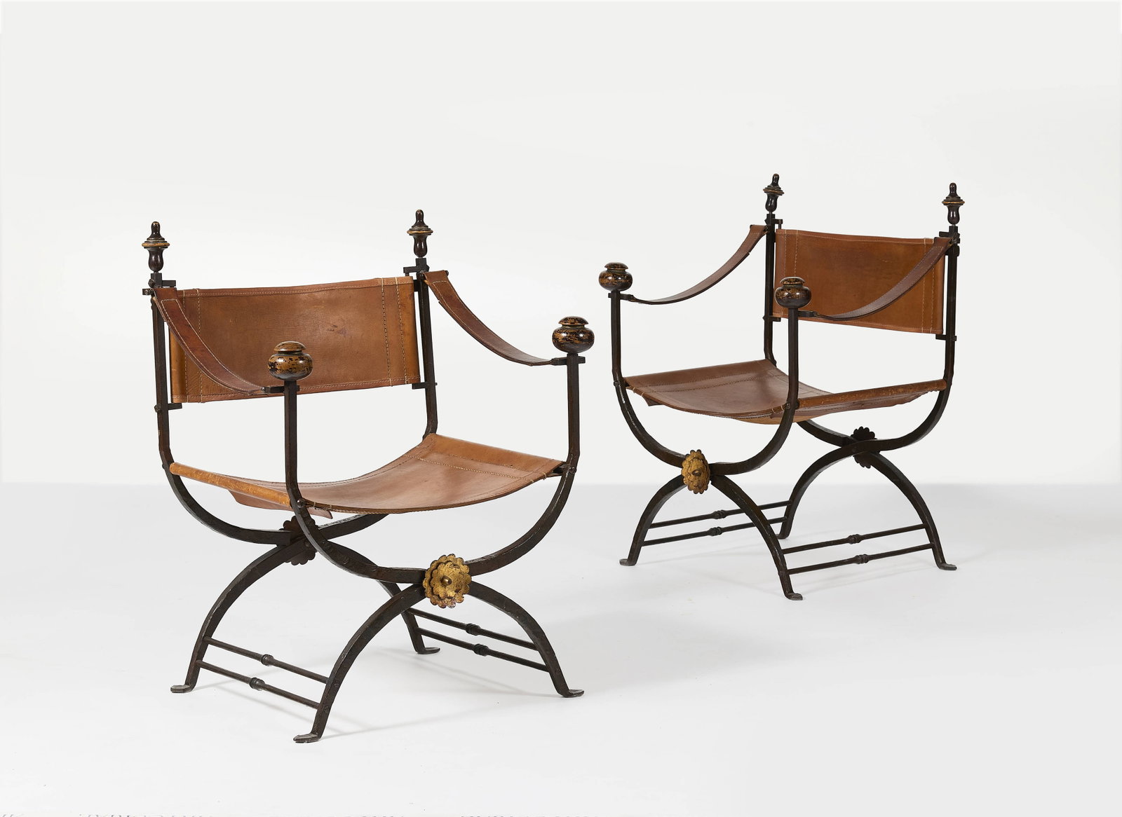 TRAVAIL ITALIEN: TRAVAIL ITALIEN Paire de fauteuils curules – circa 1960 Structure en fer forgé, assise et dossier en cuir cognac surpiqué, décorés d’une fleur en fer doré et dR