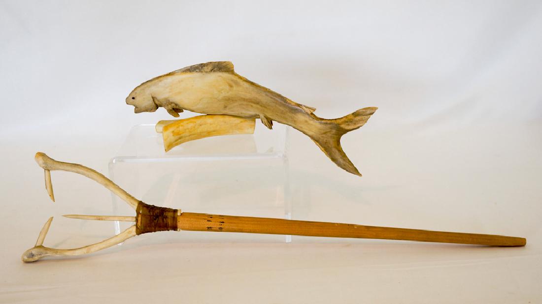 Alaska Bone Carving and Fish Hook: Alaskan carved bone fish on stand signed John Catholique and an unsigned fish hook tied to wood handle. Fish carving measures 3.25" x 9.25" x 4". Hook measures 18" x 4" x .75. Hook itself measures 5.5