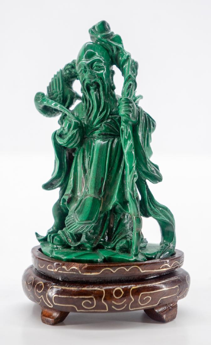 Chinese Malachite Scholar Figure: Carved Malachite standing scholar figure with a crane on his shoulder, holding a peach and on an inlaid metal rosewood stand. Carving measures 3 7/8" x 2 3/8" not counting the stand height. We ship mo