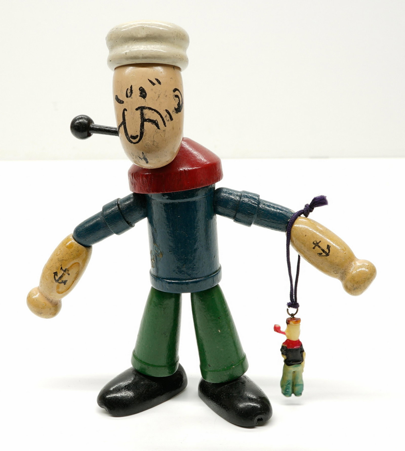 A Wood Jointed Popeye: A wood jointed Popeye figure and a small Popeye plastic charm. If lot is absent of a condition report a condition report may be requested via email. Condition report is provided as an opinion only and