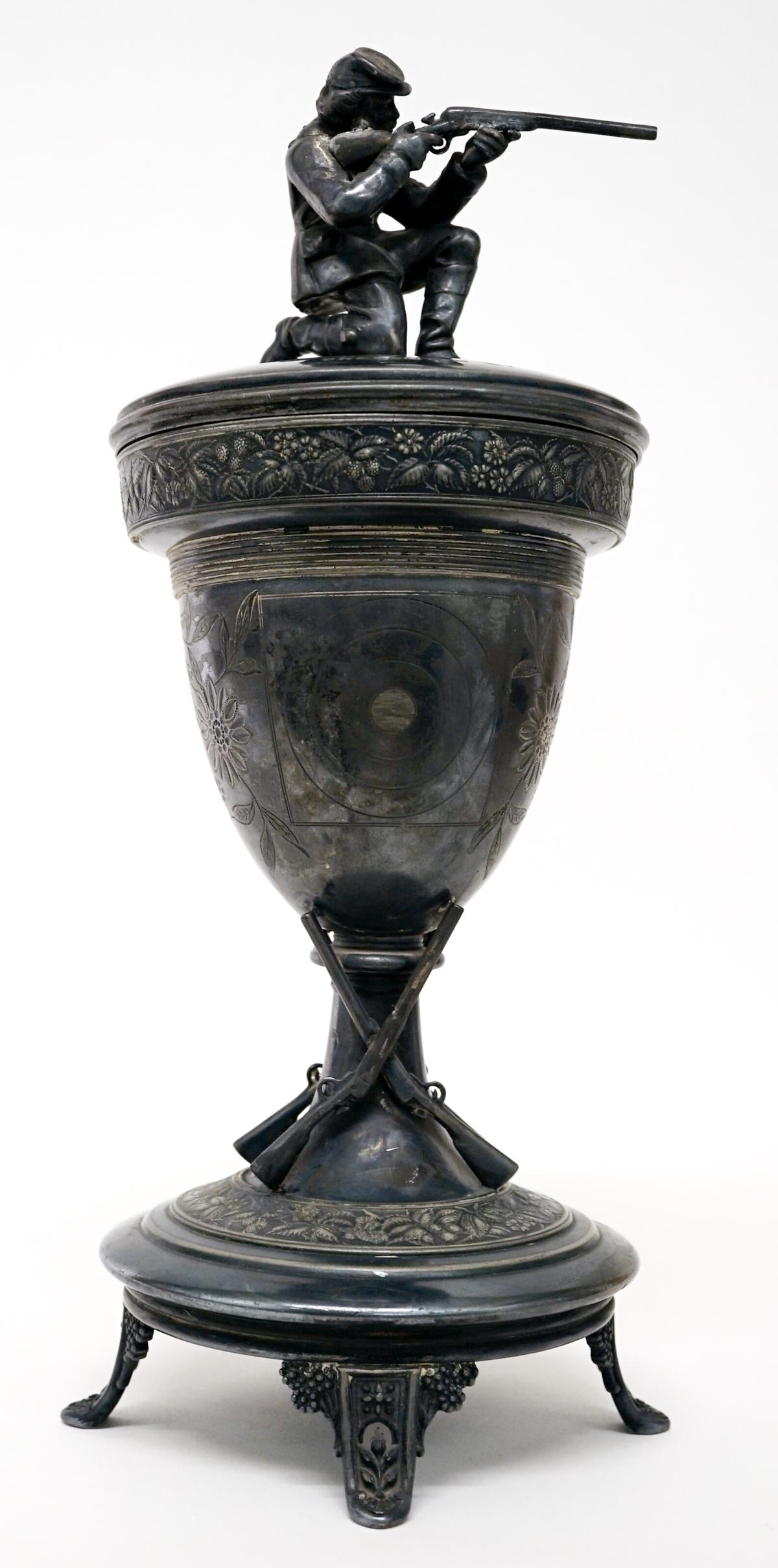 1892 Rifle Club Loving Cup Trophy: 1892 Rifle Club shooting loving cup trophy. Shooter finial is slightly caved in. Measures 14-in. x 5.5-in. G-VG/VG condition. Provenance: Bob Borcherdt collection, Bigfork, Montana. If lot is absent o