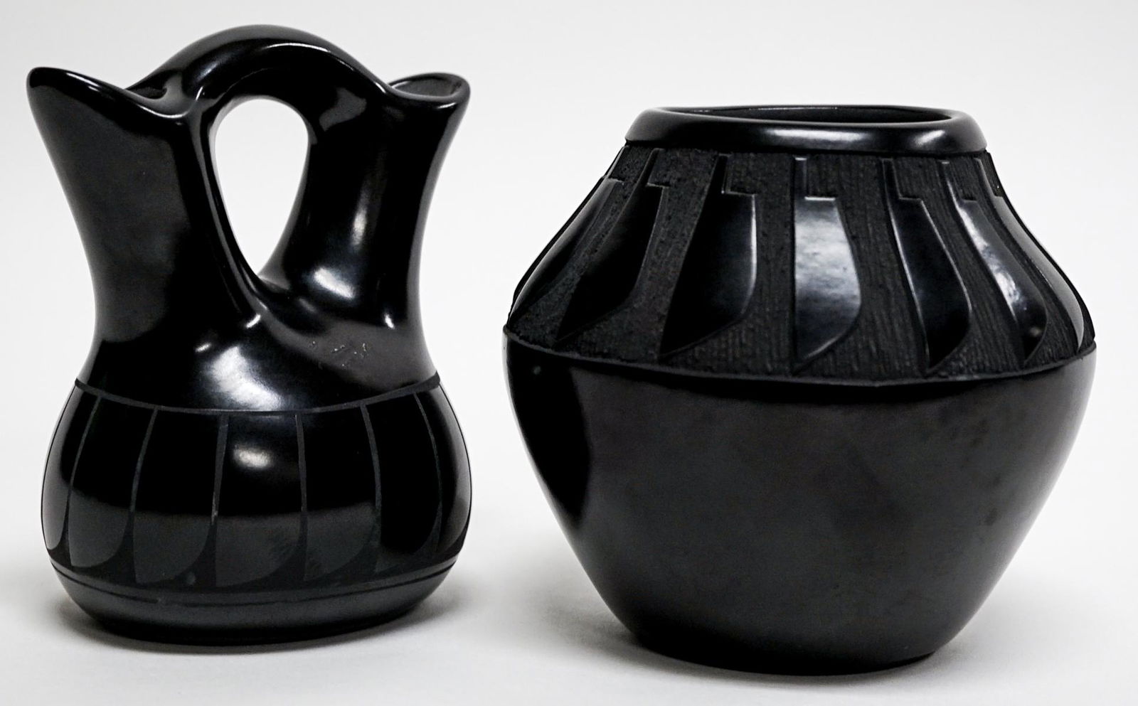 Adakai Navajo (2) Black Pottery Feather Design: Two (2) Adakai Navajo black pottery vases with feather designs. Measure 5 in. - 5.5 in. tall x 4.5 in. - 5 in. wide. Weigh 2 lbs. 8 oz. If lot is absent of a condition report one may be requested via