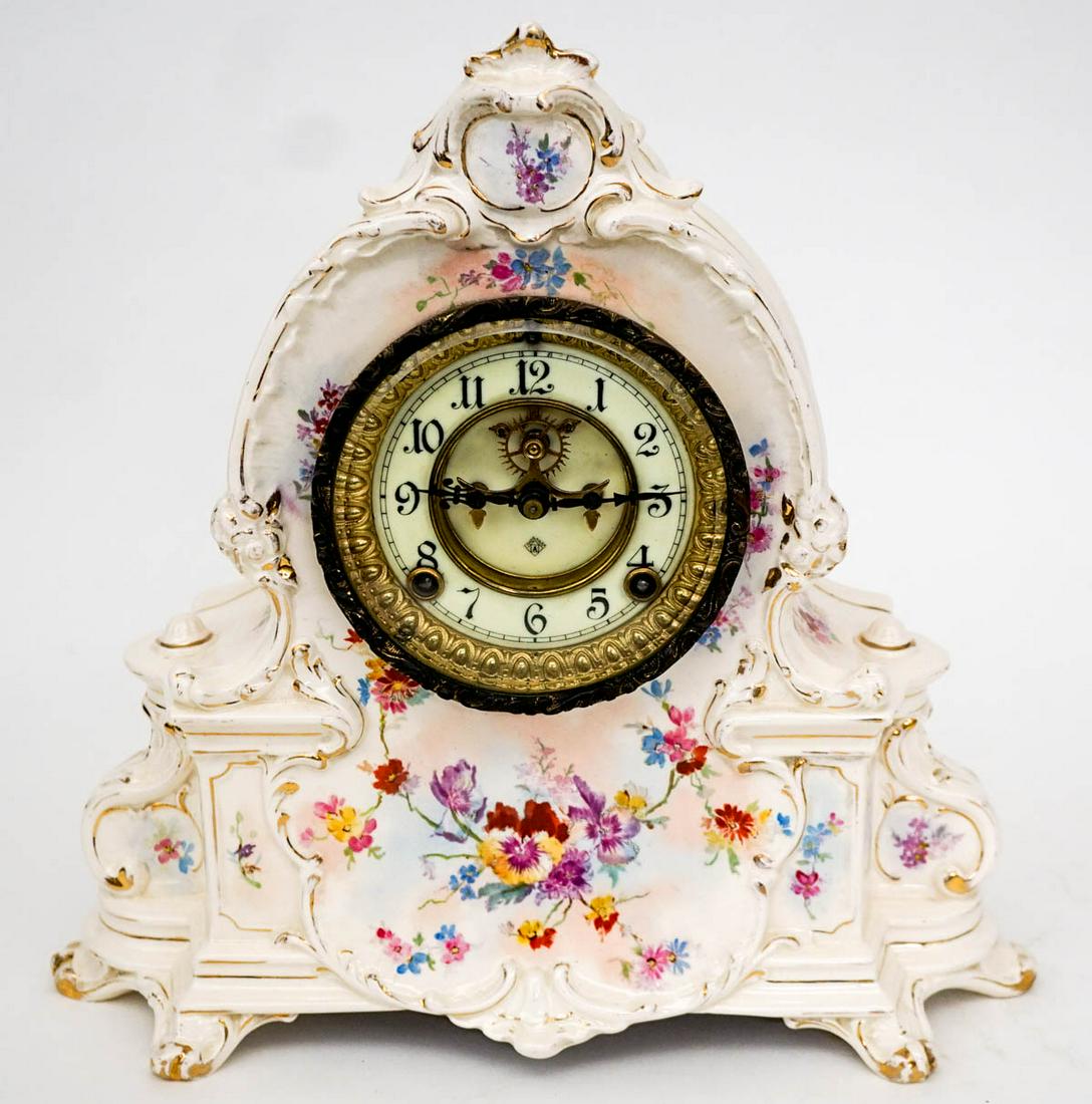 Ansonia China Case Clock [Floral]: Ansonia china case shelf clock with floral pattern against a cream colored back ground with gilt trim. Working condition. Measures 13.75 in. x 14.5 in. x 5 in. deep. Weighs 10 lbs. If lot is absent of