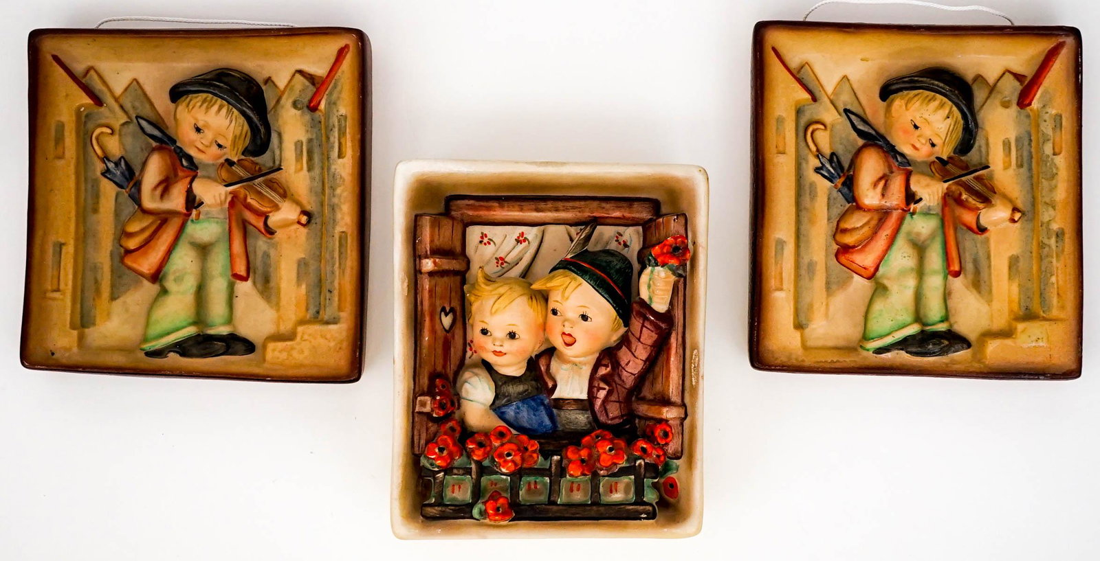 Hummel (3) Wall Plaques: Three (3) vintage Hummel wall plaques. Includes: Two (2) Little Fiddler, measure each 5 in. x 4.625 in. x .75 in.; and Boy and Girl Vacation Time, measures 5.125 in. x 4.25 in. x 1.375 in. If lot is a