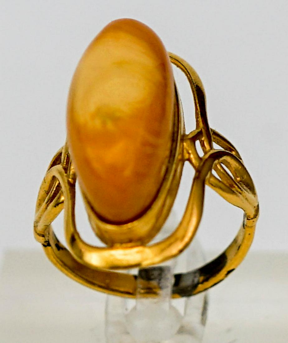 An Amber Ring Set in Yellow Gold: An amber ring set in yellow gold. Head of ring measures .875 inches x .375 inches (23 mm x 9 mm). Parts of setting test 18k and higher, other parts test negative for gold. Weighs 4 grams. Sold as-is. 