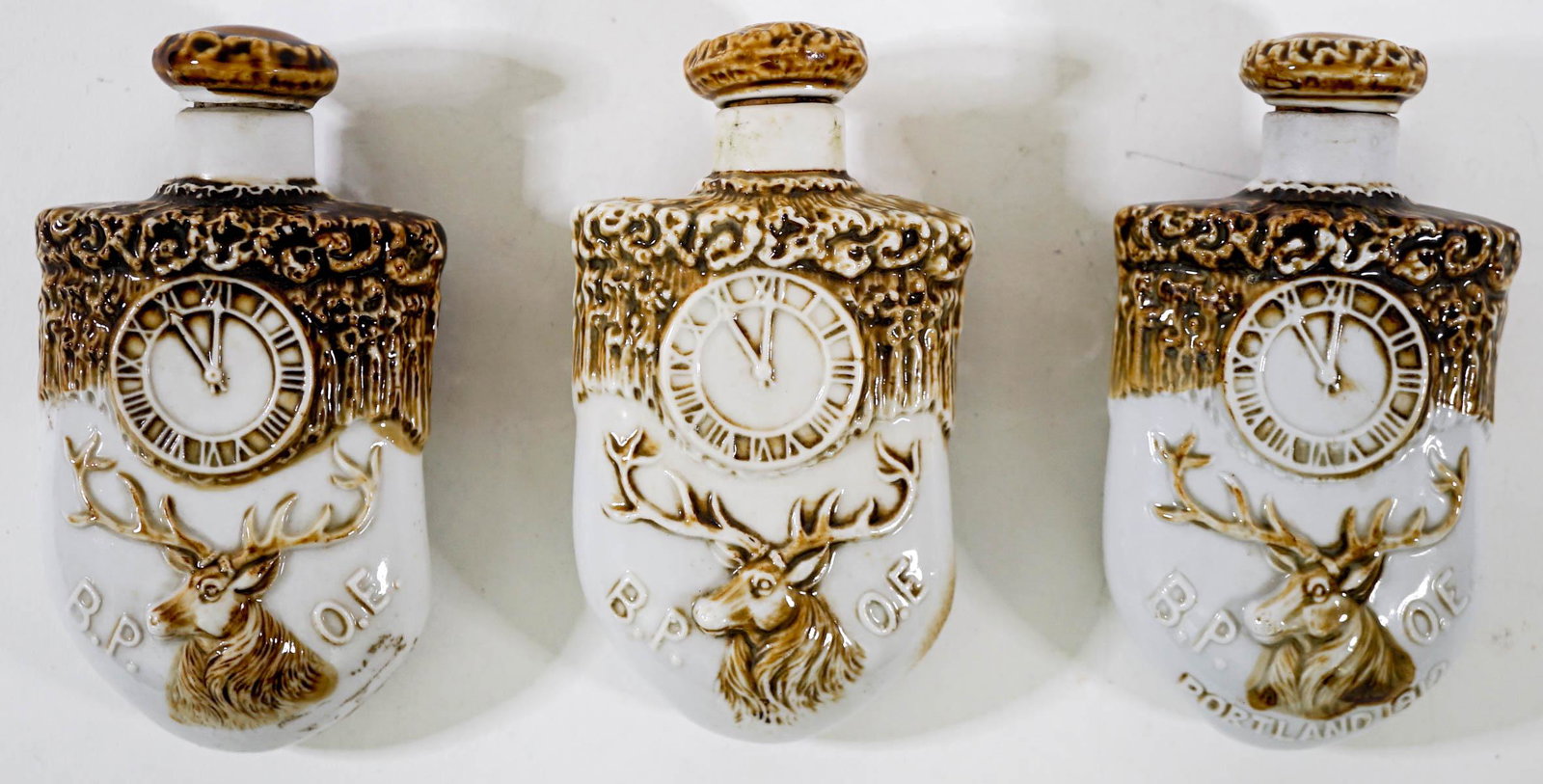 Antique (3) BPOE Porcelain Flasks: Three (3) antique BPOE porcelain flasks in the shape of an elk tooth. One is marked Portland 1912, one is marked Compliments of C. J. Stubling and one is plain. All with stoppers. Note one stopper top