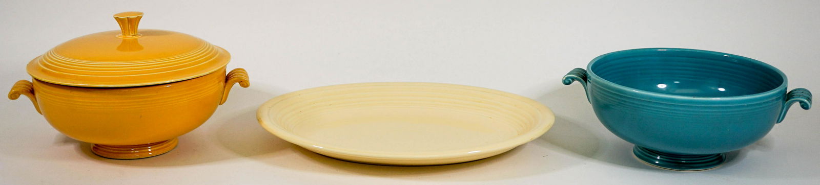 Fiesta Serveware {Platter; Vegetable Bowls]: Three (3) Fiesta serveware. Includes:12.5 inch ivory color platter; 8 in. blue vegetable bowl (note stained handle and stain at bottom); and 8 in. yellow covered vegetable (wear to rim of lid). No evi