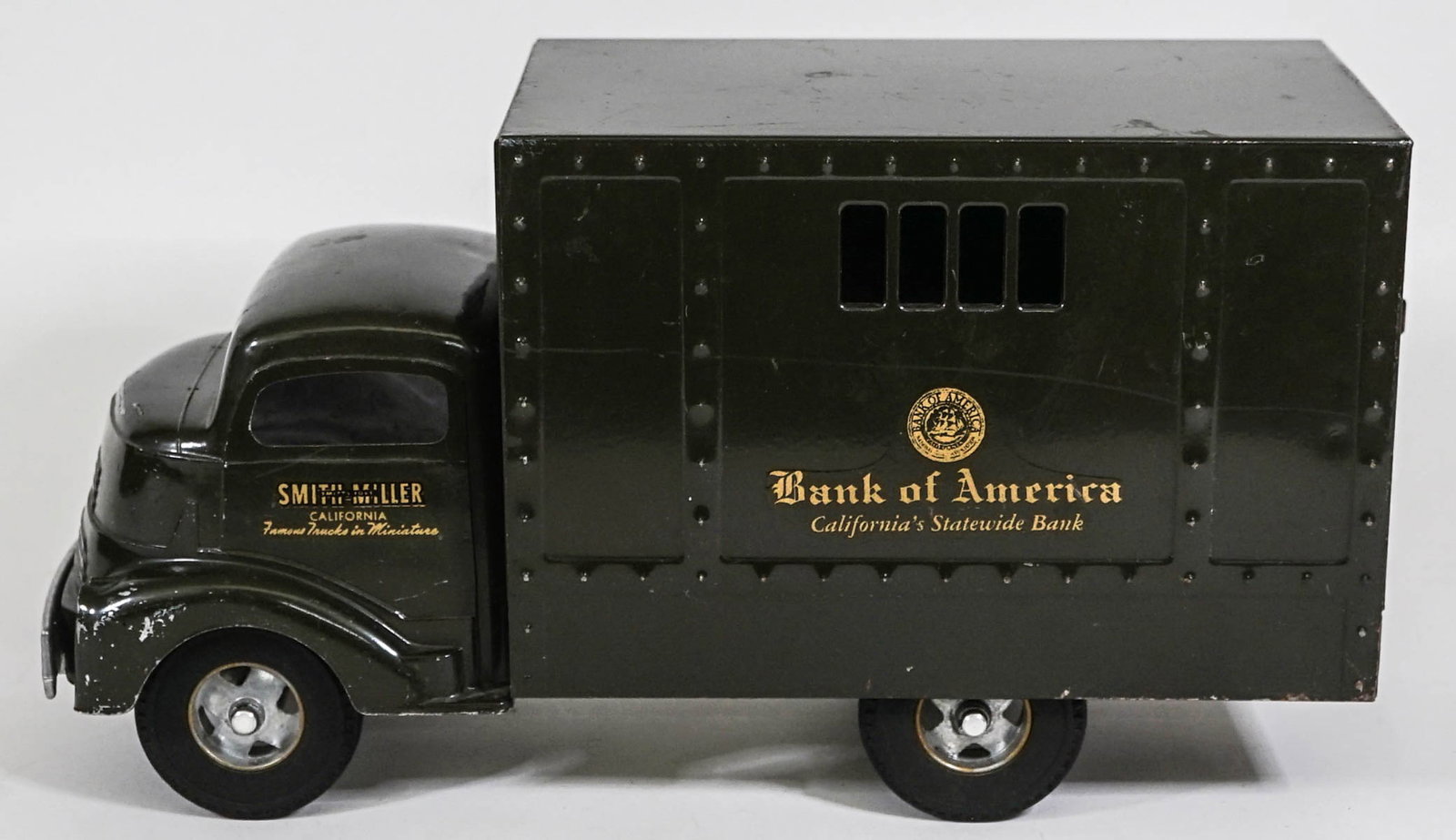 Smith Miller Bank of America Armored Toy Car: Smith Miller Bank of America Armored toy truck measures 14 in. long and is made of pressed steel. Includes lock and (5) bags. Scuffs with some paint loss. If lot is absent of a condition report one ma