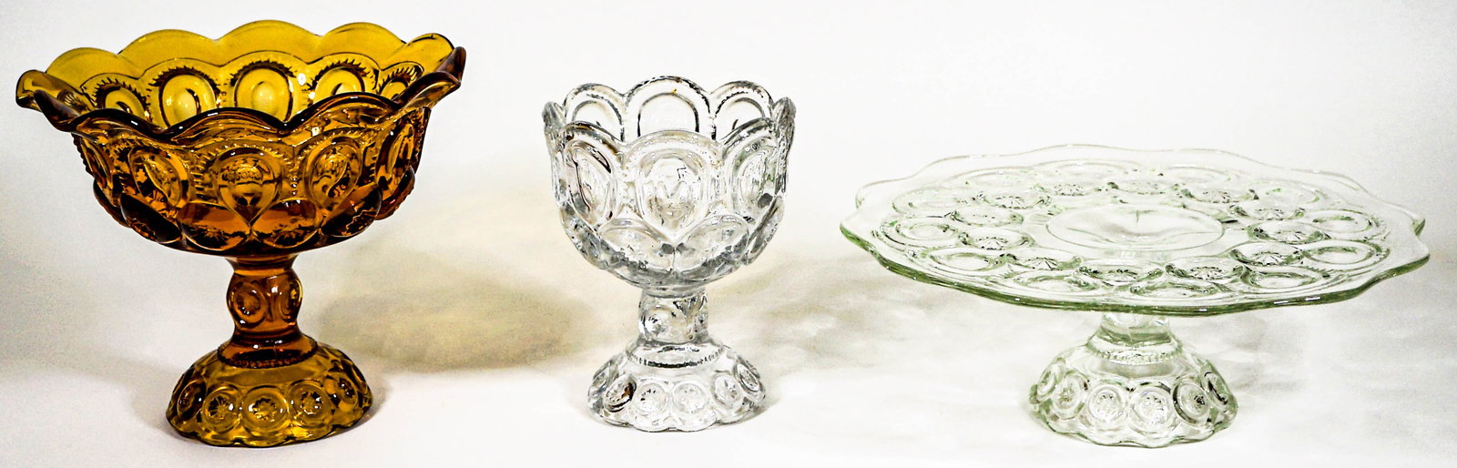 Moon and Stars (3) Serveware [Clear and Amber]: Three (3) vintage Moon and Stars glass serve pieces include: an 11 in. x 3.75 in. high clear cake stand, a 6 in. tall x 4.5 in. across rim clear compote, and an amber 6.25 in. tall x 8 in. across scal