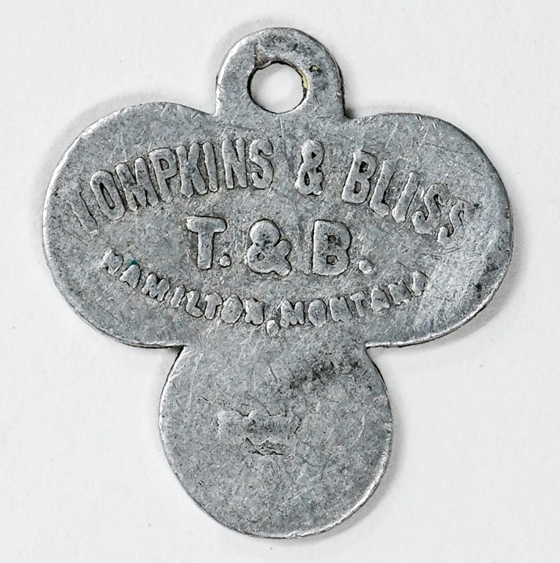 Tompkins & Bliss Saloon Hamilton, Montana: Tompkins & Bliss T & B Saloon Hamilton, Montana (clover-shaped). Good for 5c in Trade. VG/VG+ condition. Measures 30 mm x 27 mm. If lot is absent of a condition report one may be requested via email. 