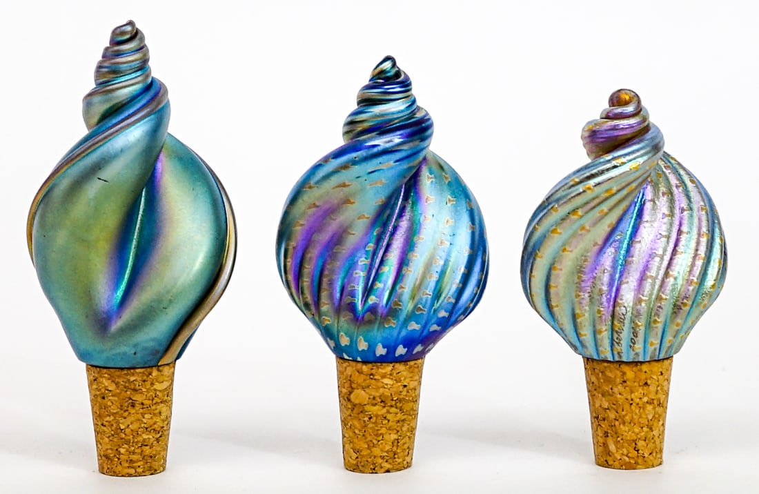 Stuart Abelman (3) Art Glass Bottle Stoppers: Three (3) iridescent art glass bottle stoppers in the form of sea shells. Measure 3.5 to 4 in. tall x 2 x 1.5 in. No evident cracks, chips or repairs. Measures 5 x 7 x 1.5 in. for shipping purposes on