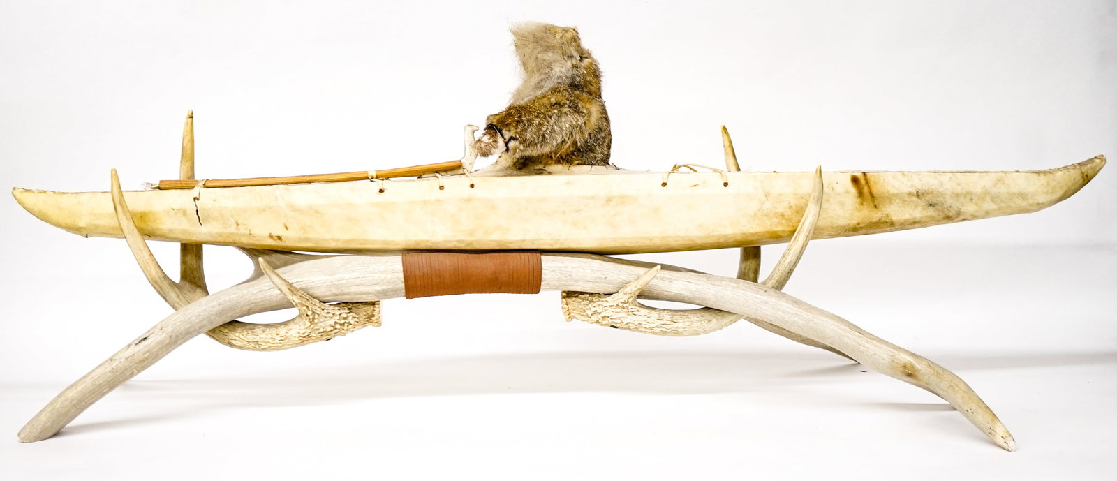 Inuit Skin Kayak Model on Custom Stand: Inuit Skin Kayak Model on Custom Antler Stand. On antler base measures 40 x 12 x 16 inches. There is loss and looseness to the rabbit fur covering the human figure leading us to catalog the human figu