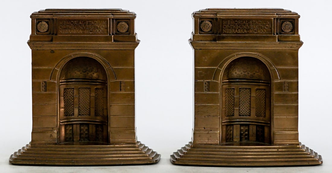 University of Nebraska Memorial Stadium Bookends: Pair of University of Nebraska Memorial Stadium MCMXXIII. Cast metal with brass finish. Bookends EACH measure 5 x 5 x 1.5 in. Lot measures 5 x 5 x 3.5 inches for shipping purposes. The absence of a co