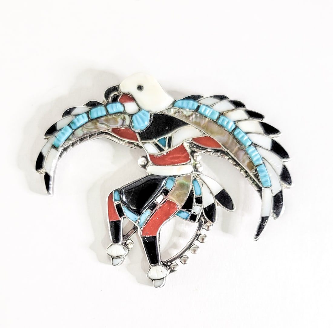 E. Luben SIGNED Zuni Eagle Dancer Brooch: Zuni Eagle Dancer silver with inlaid turquoise, coral and Mother of Pearl brooch. Signed E. Luben on verso. Measures 3.25 in. wide x 2.5 in. Weighs 26 grams. Lot measures 5.5 in. H x 6.5 in. W x 6.5 i