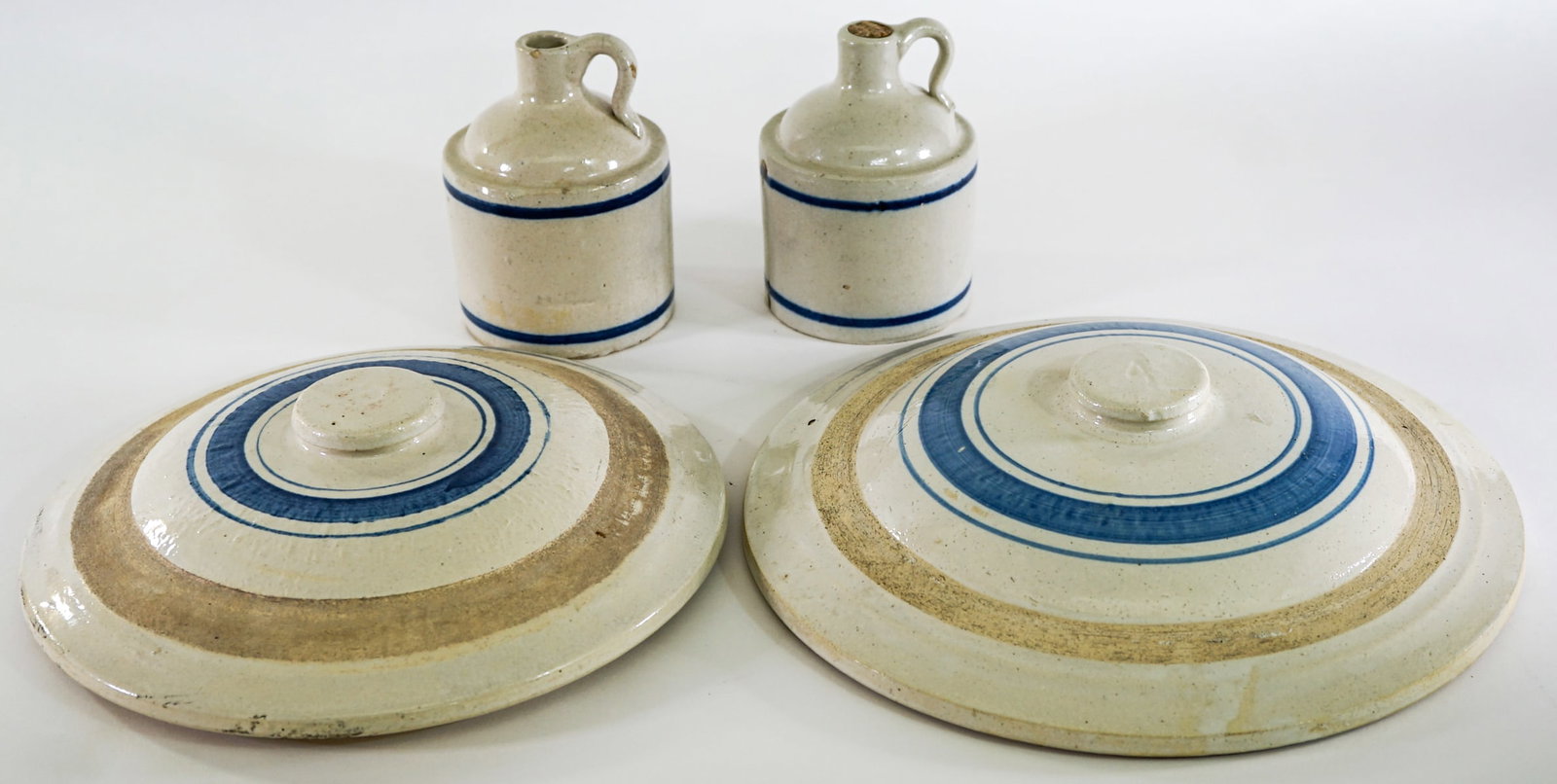 Blue Ring Crock (2) Lids (2) Small Jugs: Lids measure 10.25 to 12 in. diameter; (2) 5.5 in. jugs. Lot measures 5.5 in. H x 14 in. W x 14 in. D for shipping purposes only. The absence of a condition report does not imply that the lot is in