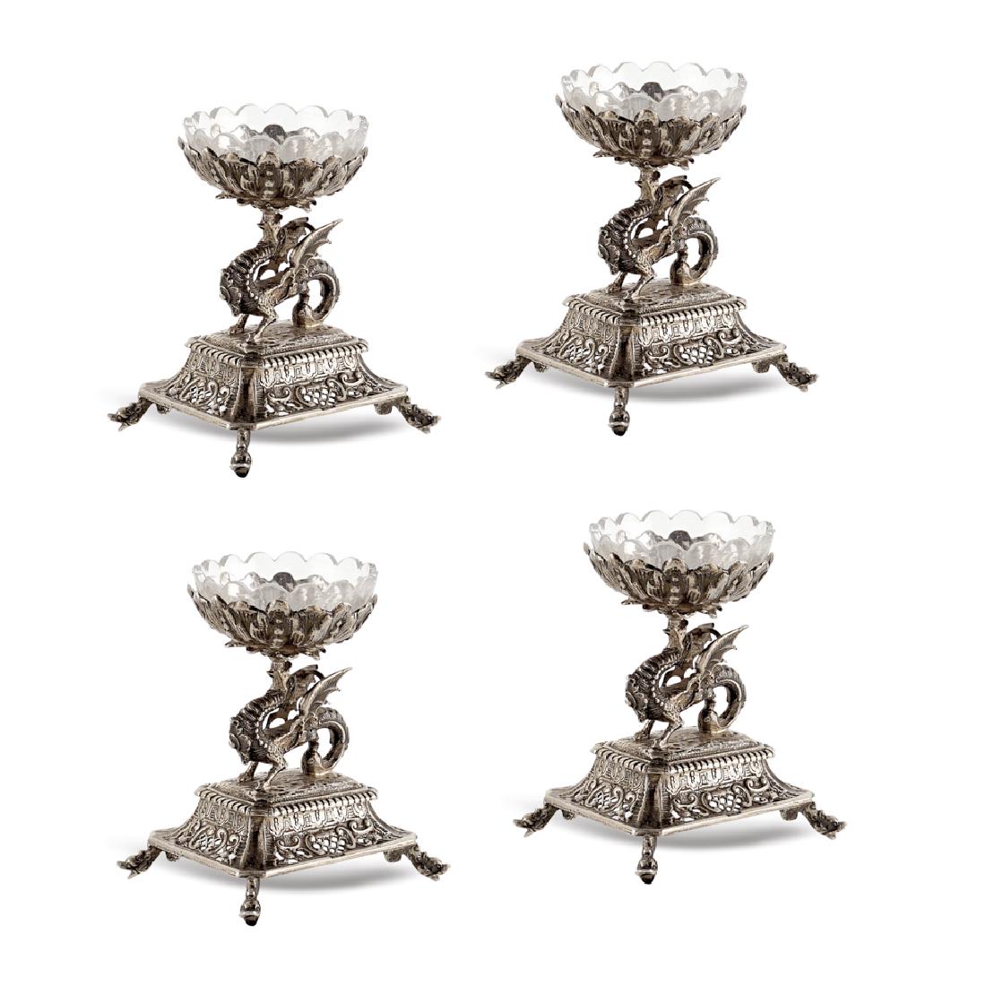 Set of four silver salt cellars Germany,: early 20th century, weight 492 gr., Friedrich Reusswig goldsmith, squared base resting on four feet, winged dragon modelled supporting a floral cup, an interior glass cup is missing, h. 9 cm.