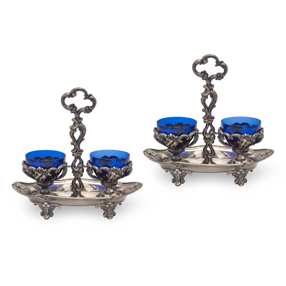 Pair of silver salt cellars (2): France, 1911-1916, 18,5x18,5x9x5 cm. each, marks of Alphonse Debain, embossed and chiseled bodies with volutes and vegetal motifs, complete with blue glass ampoules, weight 441 g 18.5x