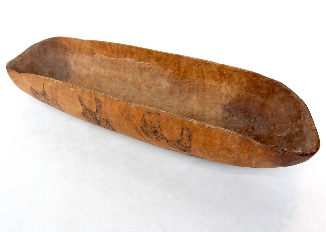 Hardwood Coolamon Pokerwork Totemistic Design: A hardwood Coolamon with pokerwork burnt in totemistic designs. Deep bowl. These were essential to Aboriginal life, and were used for gathering food, cradling infants, and storage. 21 in. x 6 in. / 53