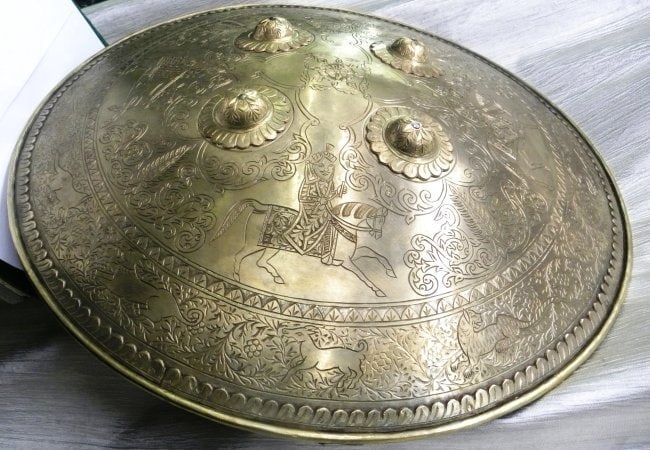 SIKH WARRIOR SHIELD 4 SIKH WARRIOR ONHORSE REPRESENTING MAHARAJA RNJIT SINGH BORDER ANIMAL: Incredible Sikh warrior brass shield 4 SIKH warriors on horse.Province : Asian. Made : Made of hand forged steel, hand hammered and chiseled. Brass plated, in convex form. A rare finding stunning Asia