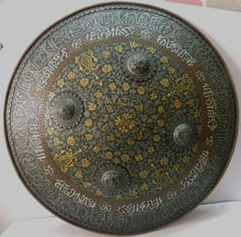 Ancient old Islamic Calligraphy Shield surface floral convex form large Surface floral & tendril: An intricately engraved circular metal shield featuring elegant Arabic calligraphy along the outer rim, combined with delicate floral and geometric patterns across its surface. The antique bronze and 