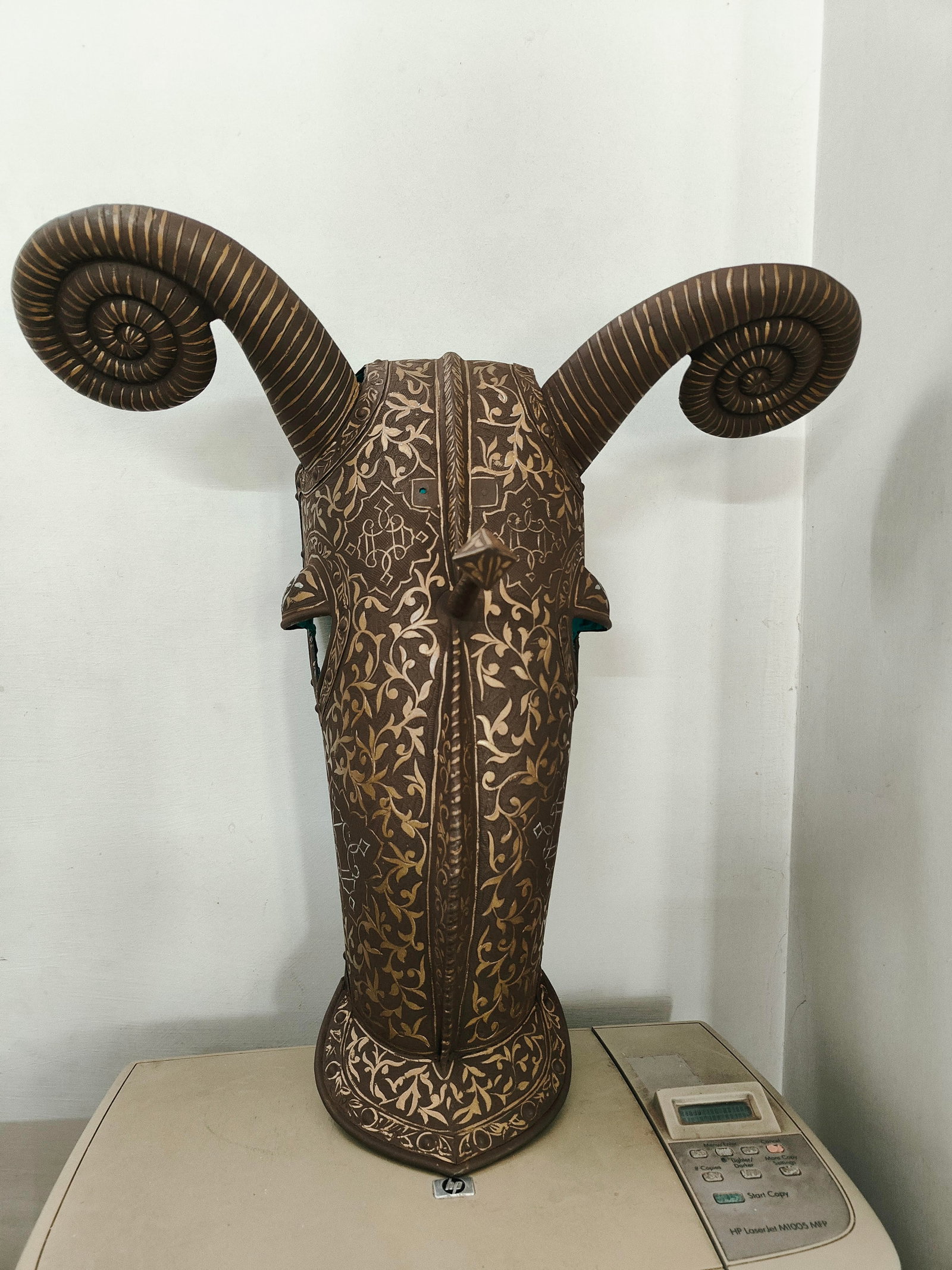 INCRDIBLE IRON ANICENT HORSE MASK EAR &EYES SHIELD SURFACE HAND ENGRAVEDFLORAL AND CREEPER DESIGN: This image features an impressive horse-head artefact adorned with intricate golden patterns on a bronze-toned surface. The large, curved horns symbolize strength, determination, and resilience. The d