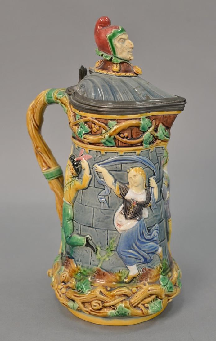 Mintons Majolica tower pitcher with cover, dancing: Mintons Majolica tower pitcher with cover, dancing figure relief and joker bust finial (chip on cover). ht. 13in.