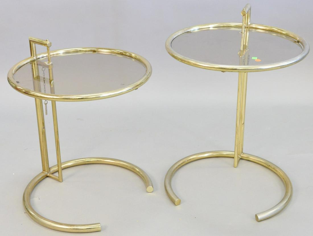 Pair Eileen Gray style adjustable tables, tubular gold: Pair Eileen Gray style adjustable tables, tubular gold tone steel, round glass top, light wear and surface scratches, each 30 1/4" x 20".
