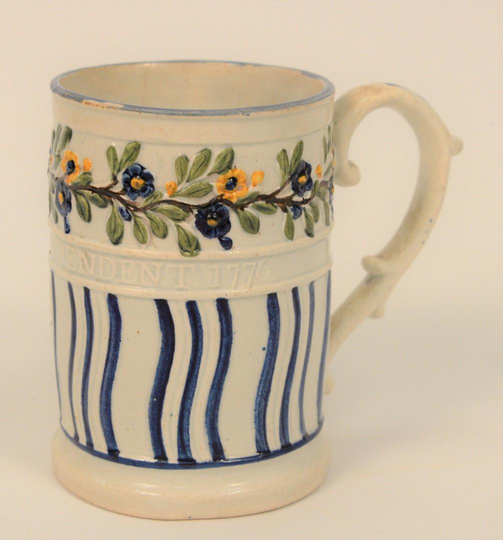 Pearlware Tankard, having raised decoration of wavy: Pearlware Tankard, having raised decoration of wavy blue lines and raised floral border, and raised American Independent 1776, (with faint hairline near top).height 4 inches.Literature: only two recor