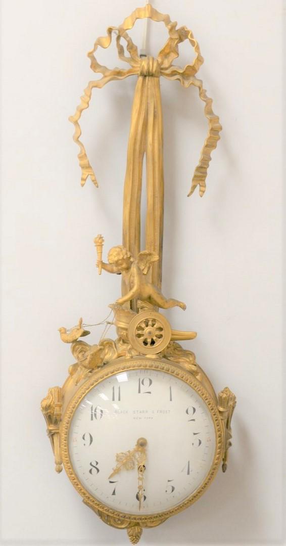 Black Starr and Fronze Bronze Figural Wall Clock having: Black Starr and Fronze Bronze Figural Wall Clockhaving gilt bronze, ruffled ribbon and bow over Putti figure, on a chariot being pulled by birds, and round enameled dialheight 35 inches
