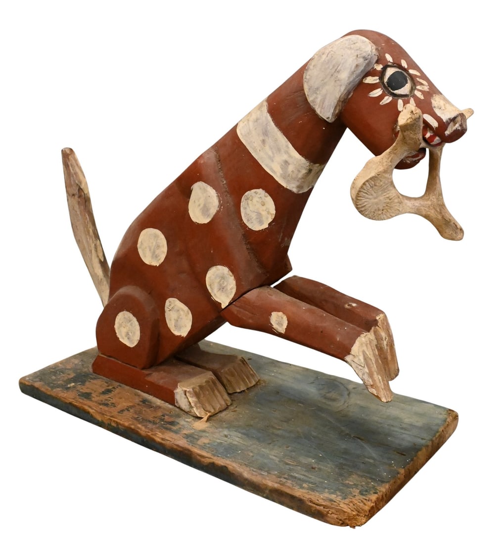 Carved and Painted Wood Folk Art Dog: Carved and Painted Wood Folk Art Dog seated position with front two paws raised and holding a bone in its mouth height 12 inches, length 14 inches Provenance: Estate of Michael and Elizabeth Ponak Pom