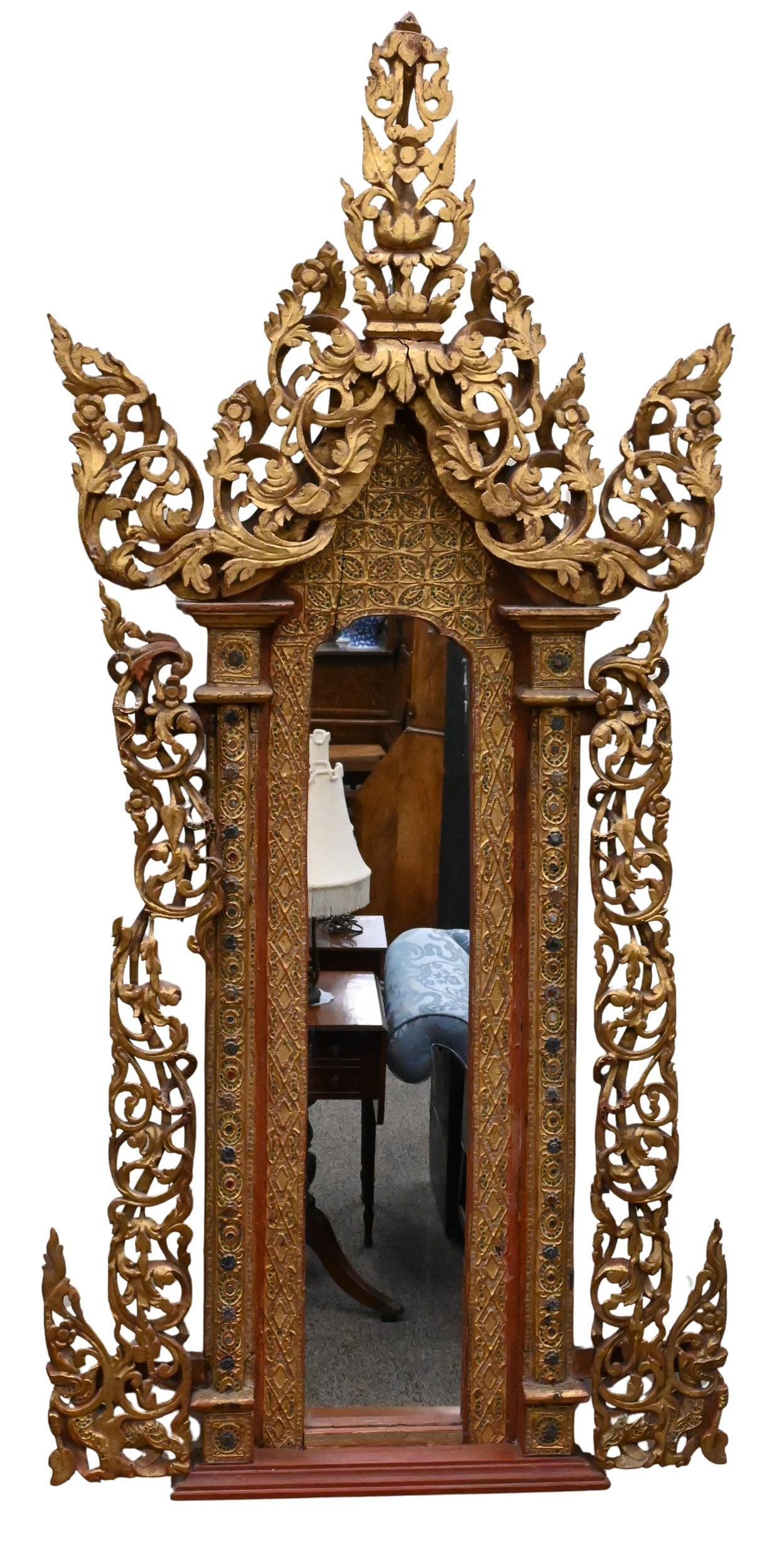 Burmese Giltwood Shrine Mirror: Burmese Giltwood Shrine Mirror having elaborately carved and reticulated scrolling vine border flanking two glass jewel inset columns and center mirror, with red painted accents 60" x 28"