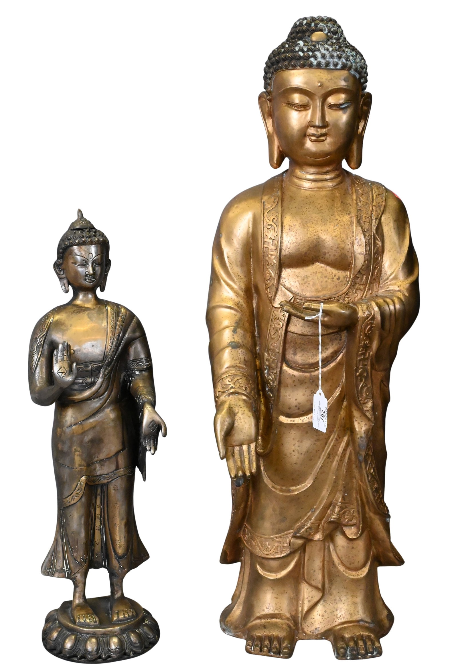 Pair of Metal Buddha Figures: Pair of Metal Buddha Figures to include one gilt metal standing Buddha figure in East Asian fashion with gilt overlay, elongated earlobes and extended palm, the other also in East Asian fashion with e