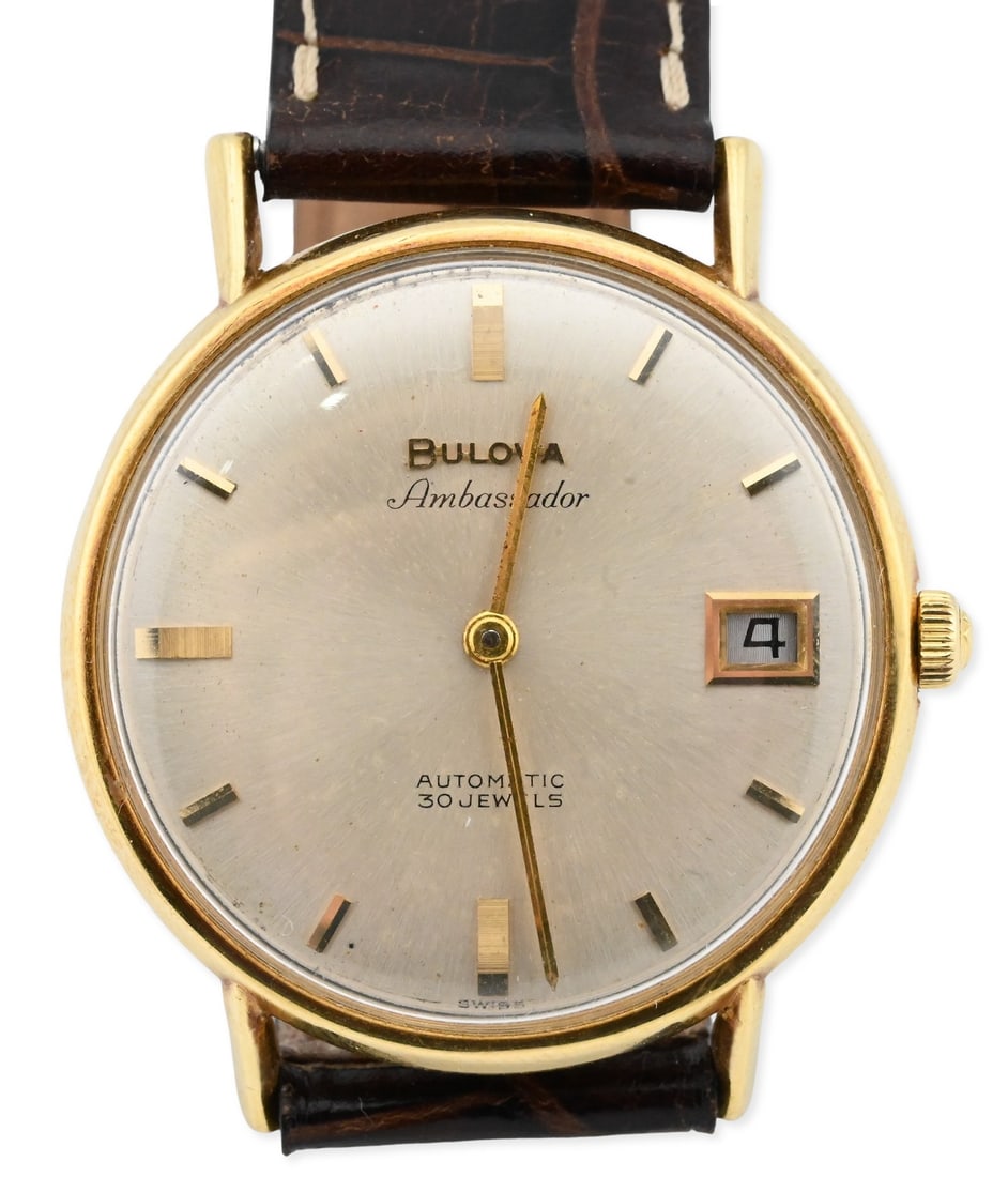 18k Yellow Gold Bulova, Ambassador Wristwatch: 18k Yellow Gold Bulova, Ambassador Wristwatch Classic round case measuring 34.6mm, the 18k yellow gold waterproof case marked on verso, serial no. 1224067. Champagne dial with applied gold baton indic