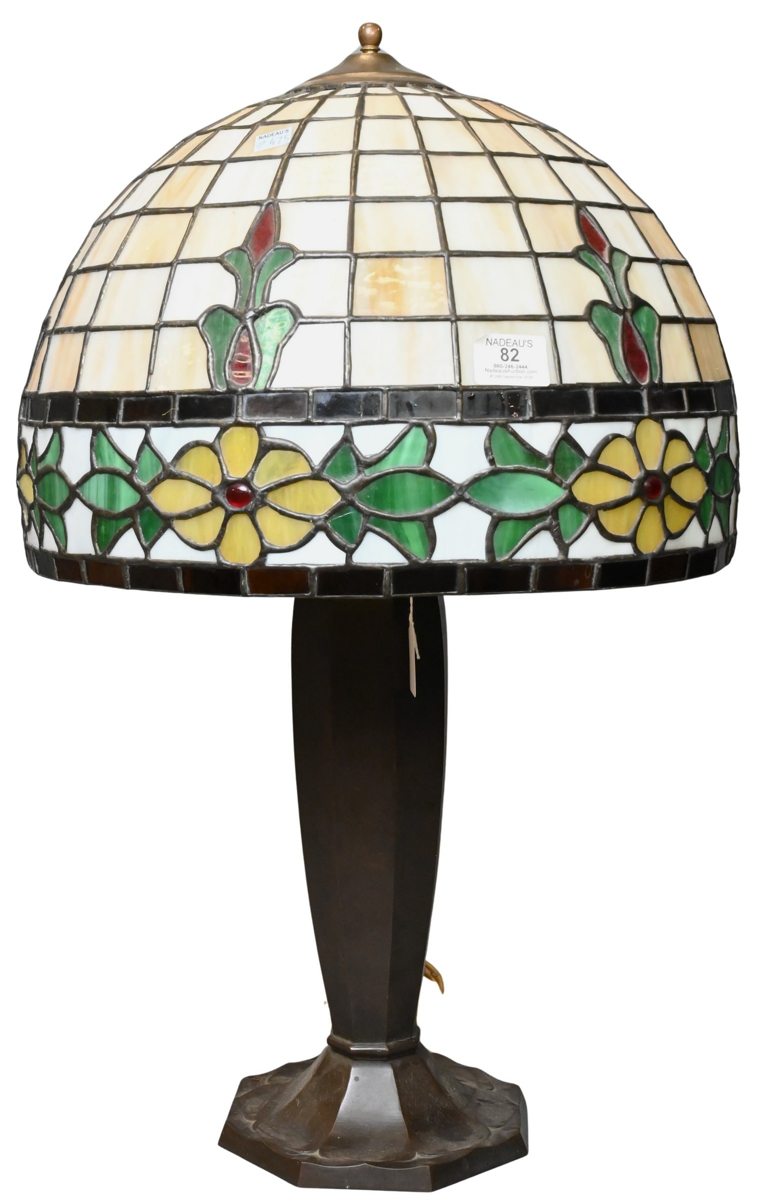 Leaded Glass Table Lamp: Leaded Glass Table Lamp having a domed shade decorated in stylized yellow flowers and green leaves beneath cream slag glass panels accented by red jewel elements, raised on a bronze faceted base,