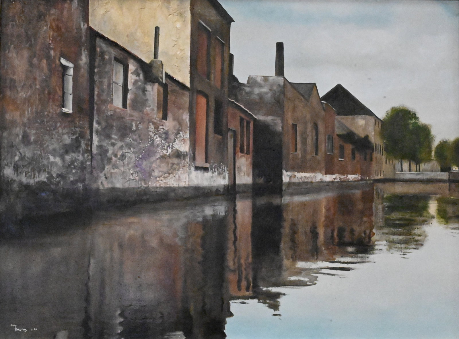 Guy Thomas (20th Century): Guy Thomas (20th Century) Industrial Canal Scene, 1982 Oil on canvas depicting industrial buildings reflected along a canal Signed and dated lower left Guy Thomas '82 23 1/2" x 31 1/2" canvas