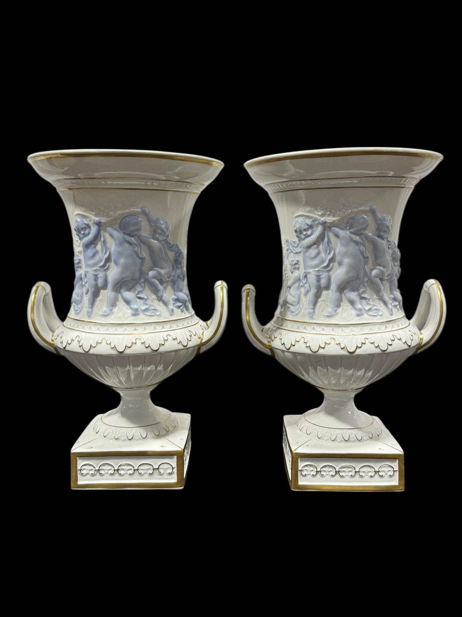 Pair of Capodimonte Cherub Urn Vases: Pair of Capodimonte Cherub Urn Vases. Light blue cherubs on both sides of vases with gold accents and double handles. Marked N with crown on the underside of both. Measures 15.5" H x 10" W x 9.25" D.