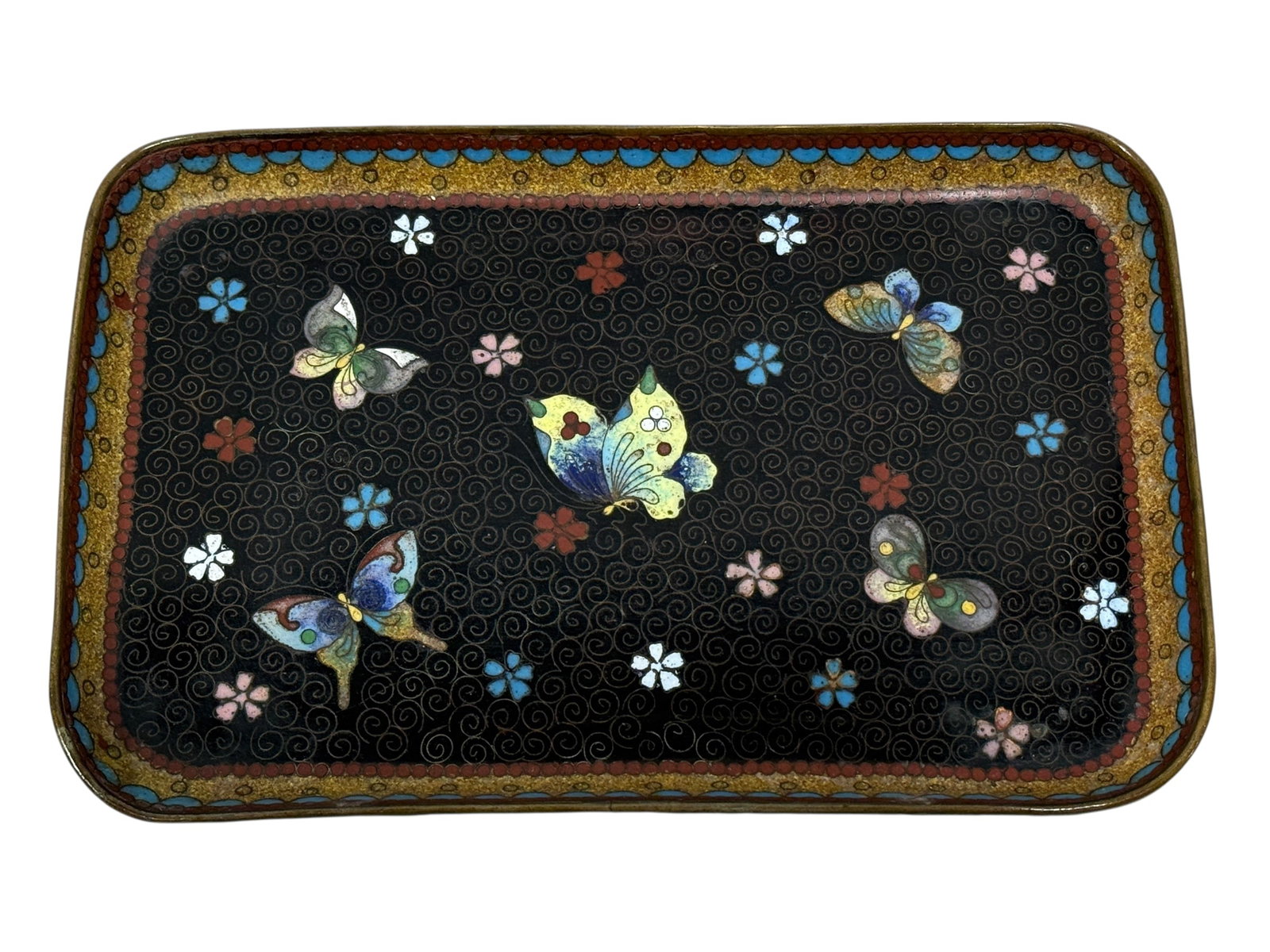 19th C. Japanese Meiji Cloisonne Trinket Dish: 19th C. Japanese Meiji Cloisonne Trinket Dish. Depicting flowers with butterflies on a black background with red, blue and gold tone borders. Measures 7.75" W x 5" D. Has some damage to enamel on unde