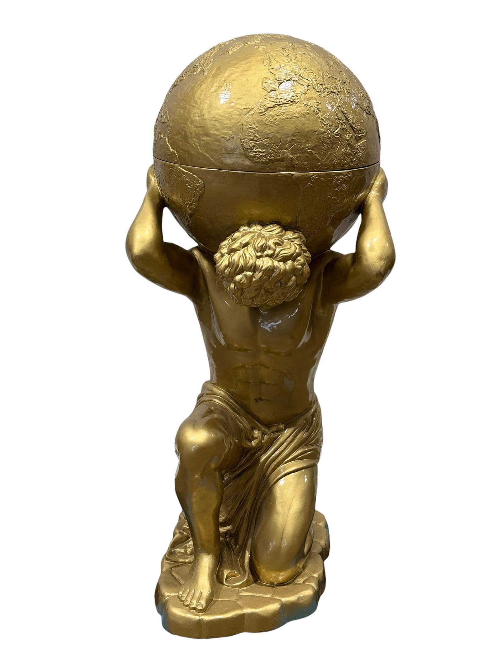 Decorative Gold Tone Atlas Figure w/ Lidded Globe Storage: This modern decorative pedestal features a kneeling Atlas-style figure supporting a hinged globe-form container. Cast in composite resin and finished in a gold-tone paint, the piece opens at the equat