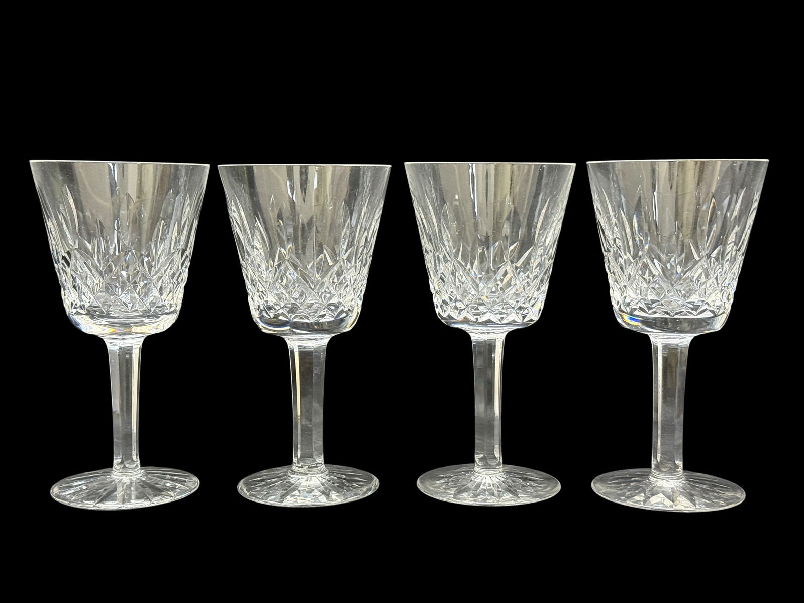 (4) Waterford Crystal Lismore Claret Wine Glasses: Elegant set of four Waterford Crystal claret wine glasses in the classic Lismore pattern, featuring deep diamond and wedge cuts around the bowls with tall, slender stems and starburst-cut bases that c
